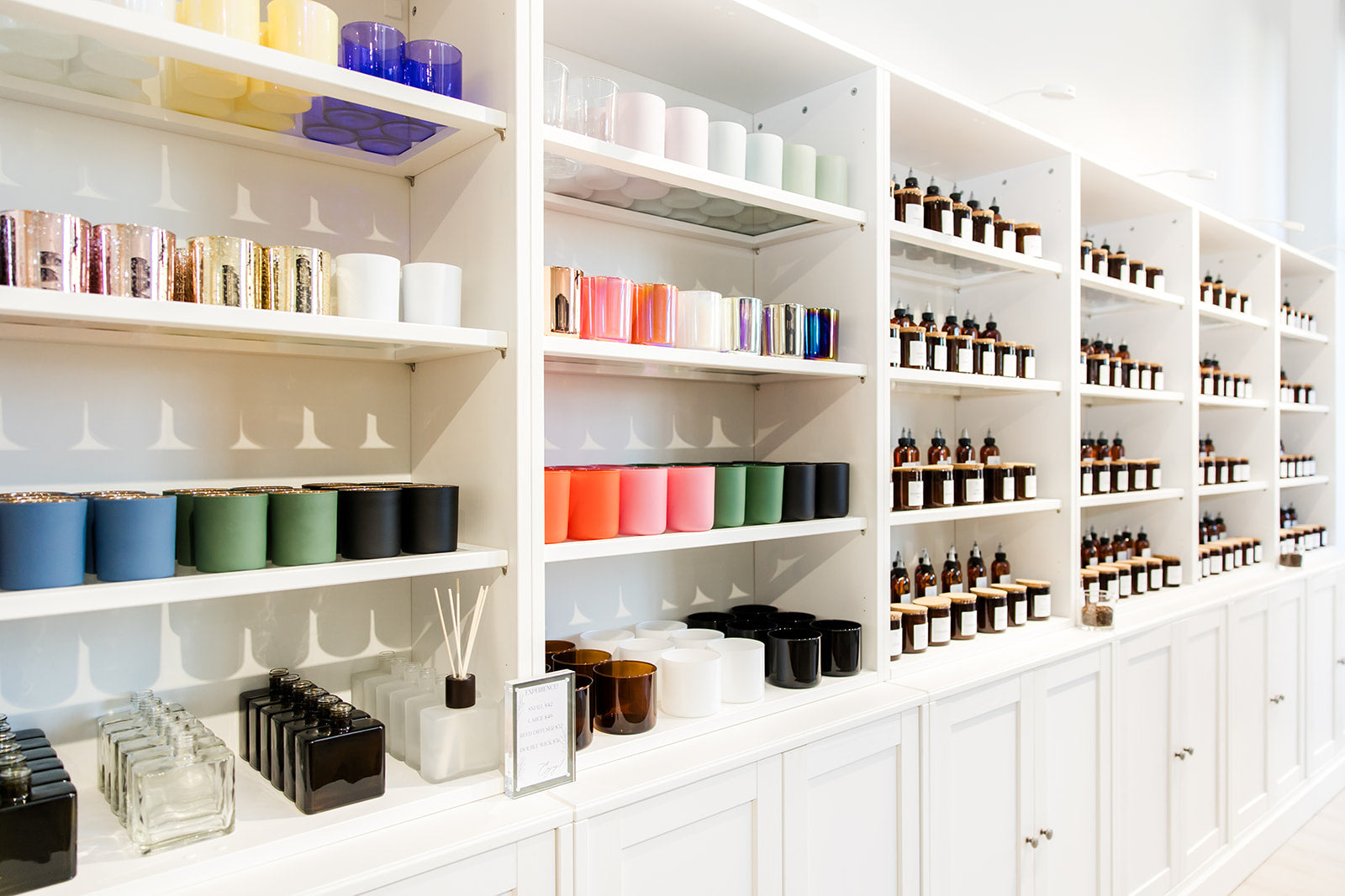 A neatly organized store shelf displaying a variety of colorful candles, glassware, and bottled products in an aesthetically pleasing arrangement.